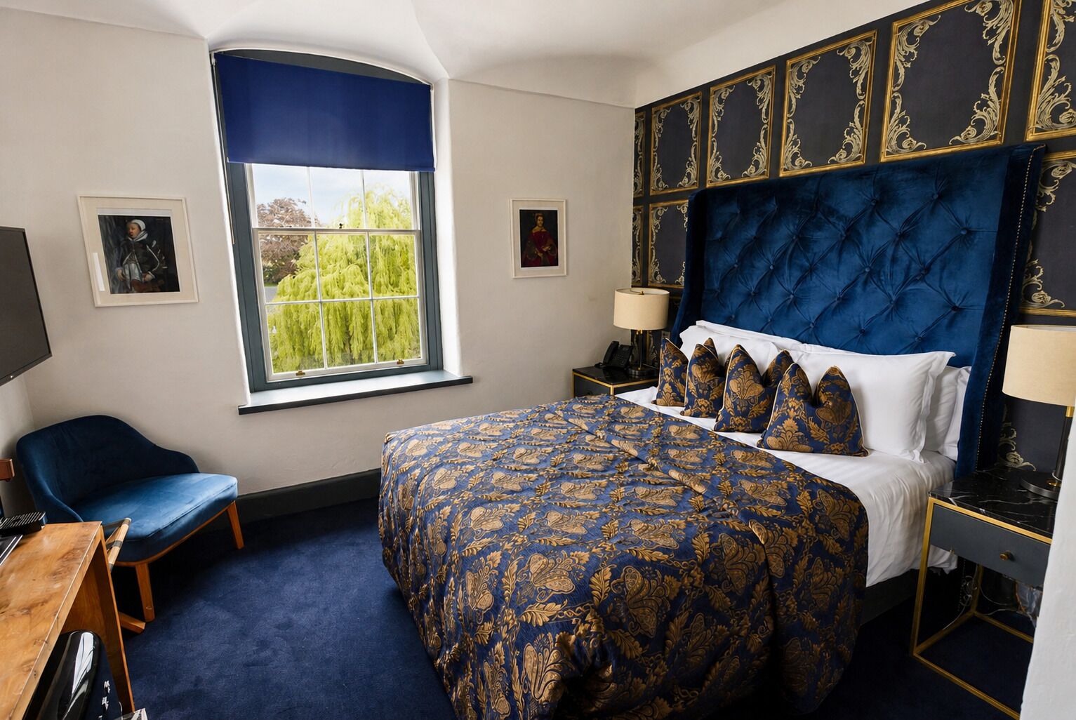 A hotel room with a large bed, a desk, a chair, and a window with a view of greenery.