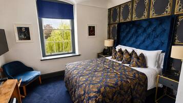A hotel room with a large bed, a desk, a chair, and a window with a view of greenery.