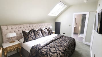 A bedroom with a tufted headboard, a bed with patterned bedding, a bedside lamp, and a skylight.