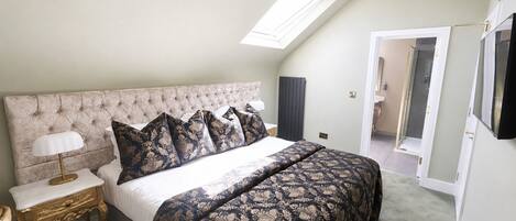 A bedroom with a tufted headboard, a bed with patterned bedding, a bedside lamp, and a skylight.