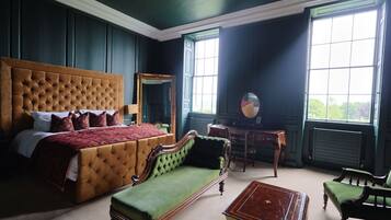 A bedroom with a large bed, a green sofa, a wooden dresser, and a mirror.
