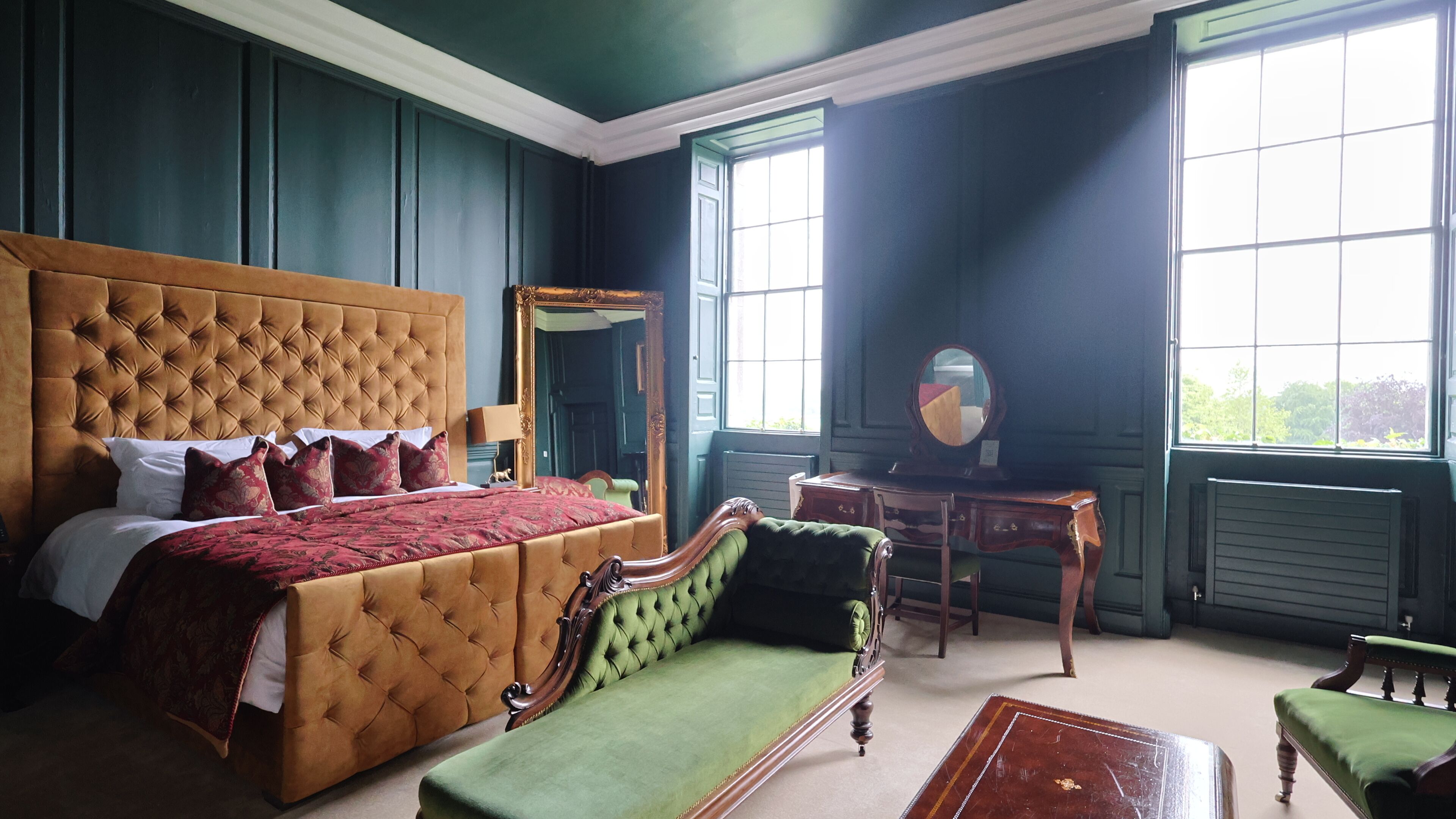 Un dormitorio con una cama grande, un sofá verde, un aparador de madera y un espejo.
