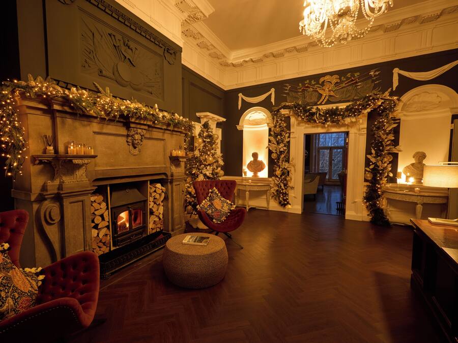 A warmly lit room with a fireplace, red armchairs, and a Christmas tree.