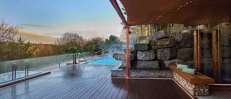 A wooden deck with a stone wall, a bench, and a view of a natural landscape.