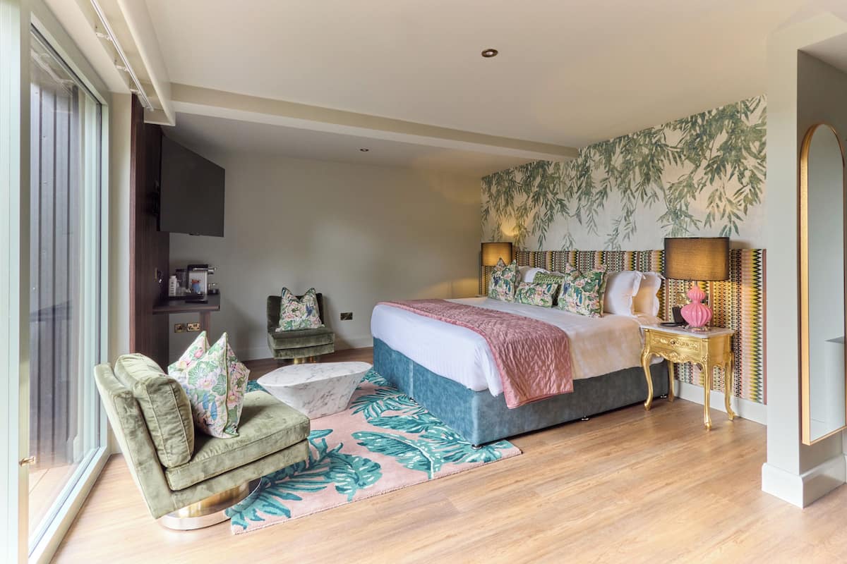 A bedroom with a large bed, a sofa, a coffee table, a TV, and a patterned wall.