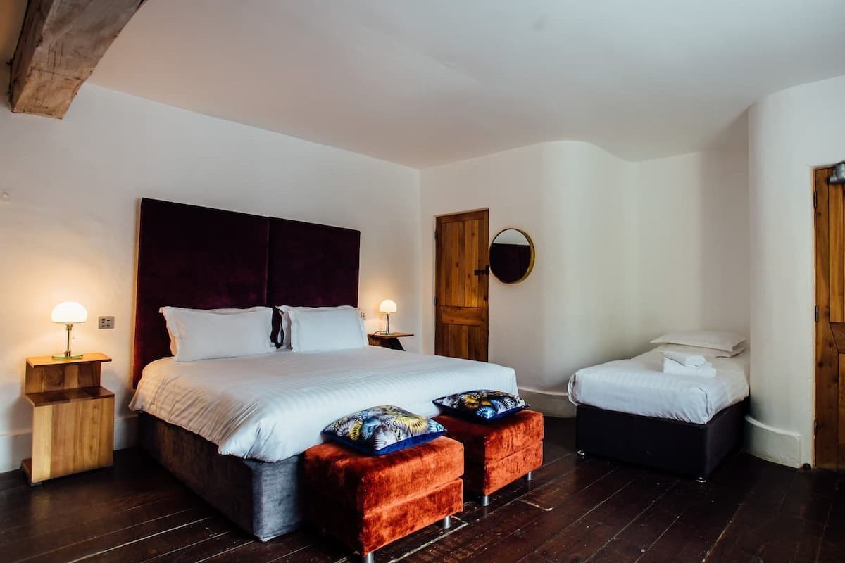 A bedroom with a large bed, two bedside tables, a wooden door, and a small bedside table with a lamp.