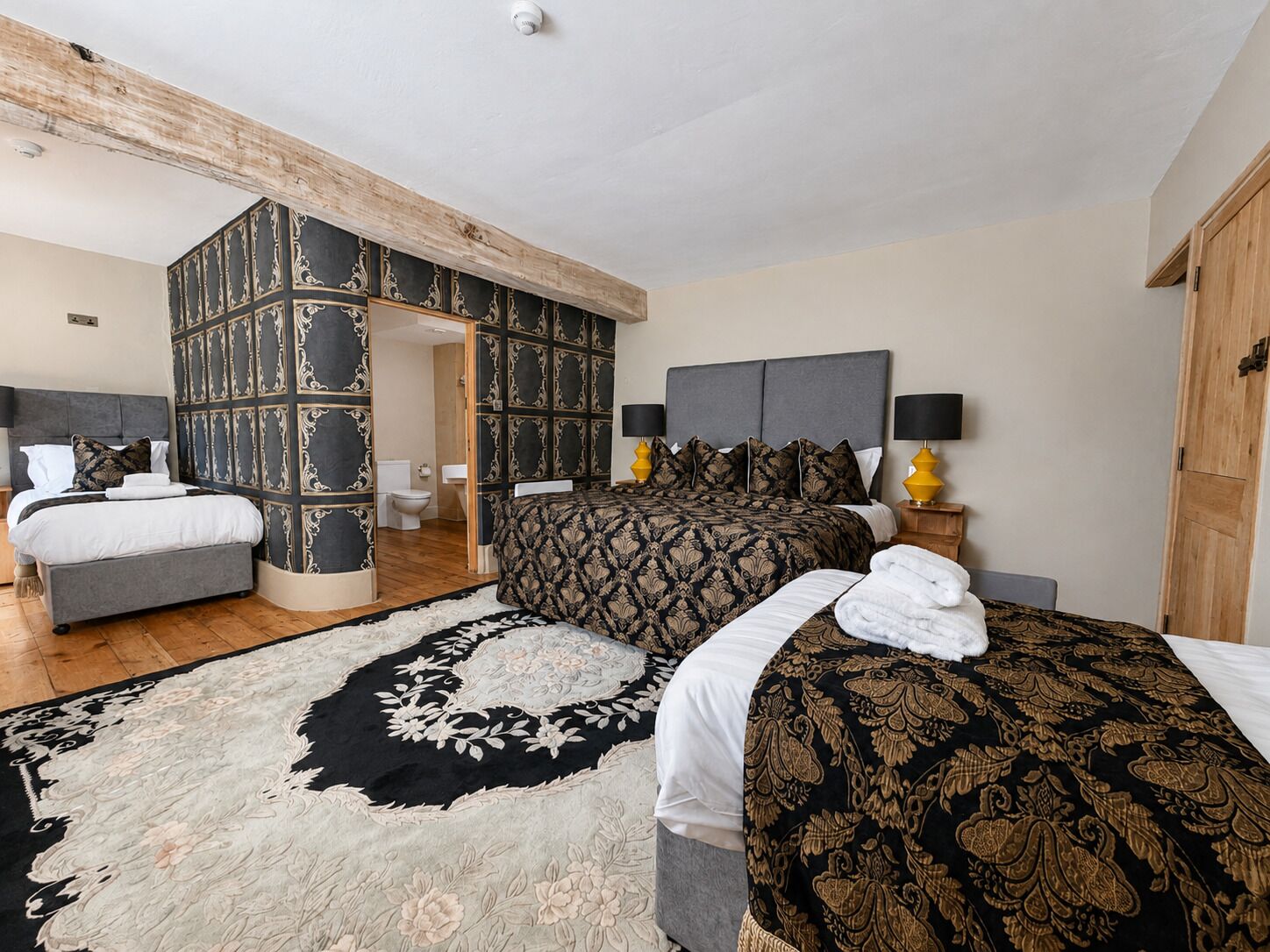 A hotel room with a large bed, a separate sofa, a bathroom, and a wooden ceiling beam.