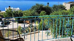 A balcony with wicker chairs, a view of the sea, and a stone building in the background. - Achlia Hotel (Ierapetra)
