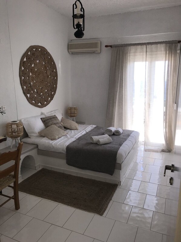 A bedroom with a bed, bedside tables, a lamp, a wall hanging, and a window with curtains.