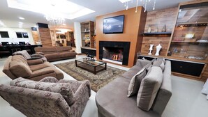 A modern living room with a fireplace, sofas, a coffee table, and a TV mounted on the wall. - Sky Ville Gramado Hotel (Gramado)