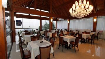 A spacious restaurant with high ceilings, wooden beams, and a chandelier. Tables are set with white tablecloths and chairs.