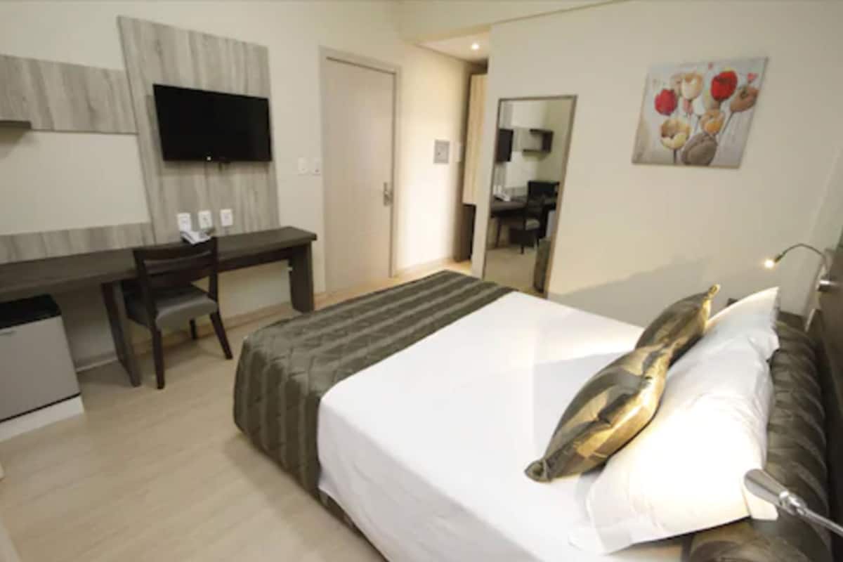 Ein Hotelzimmer mit Bett, Schreibtisch, Stuhl, Fernseher und Spiegel.