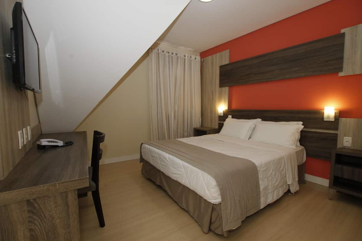 Ein Hotelzimmer mit Bett, Schreibtisch, Stuhl, Fernseher und einem fensterbepflanzten Fenster.