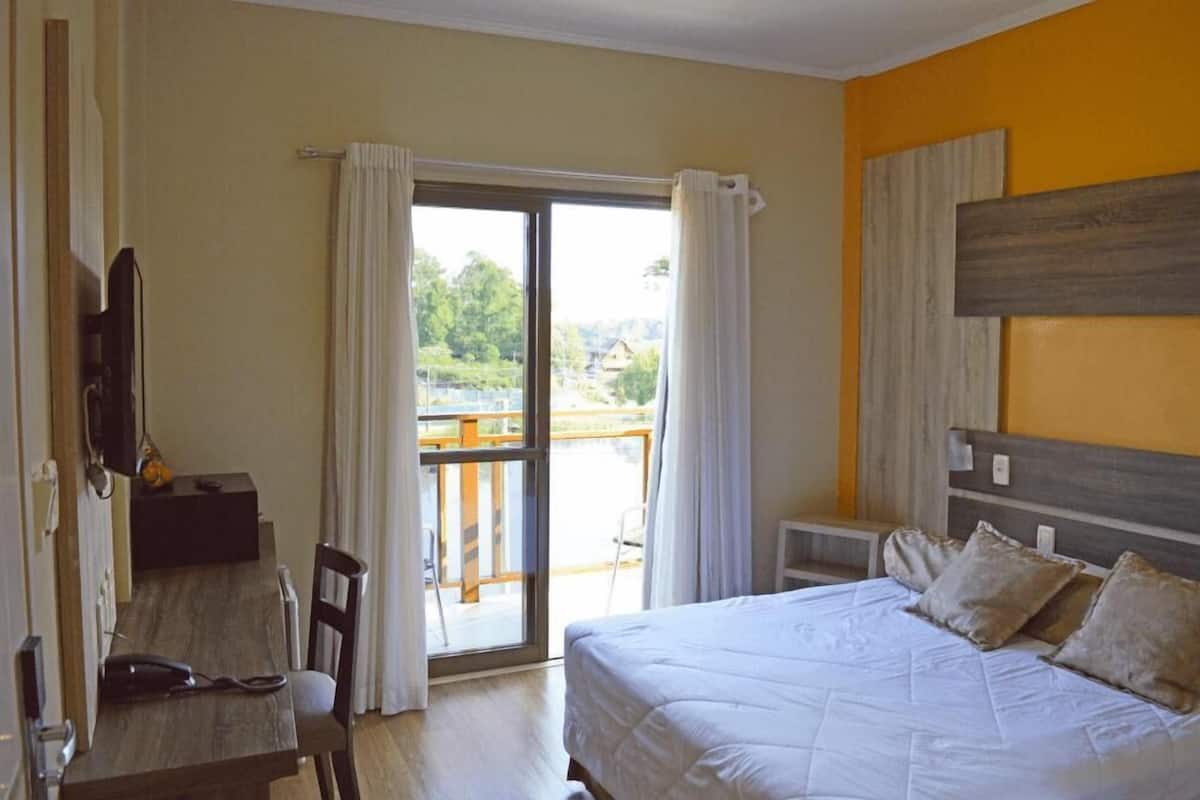 Ein Schlafzimmer mit Bett, Schreibtisch und Stuhl. Es gibt einen Balkon mit Vorhängen.