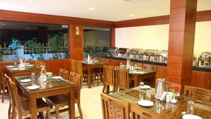 A restaurant with wooden tables and chairs, a buffet area, and large windows with a view of greenery.