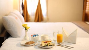 A neatly arranged breakfast table with a variety of food items, a vase of yellow flowers, and a glass of orange juice.
