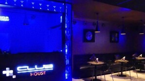 A dimly lit room with a sign reading "CLUB HOUSE" and a seating area with tables and chairs.