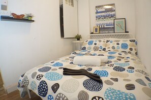 Una camera da letto con un letto coperto da una trapunta fantasia, un comodino con una pianta e una mensola a muro con oggetti decorativi.