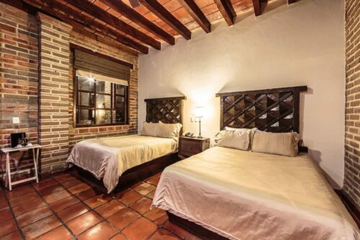 A room with two beds, a brick wall, a window, and a wooden ceiling.