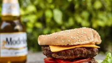 A hamburger with lettuce, tomato, and cheese, and a bottle of ModClarke beer in the background.