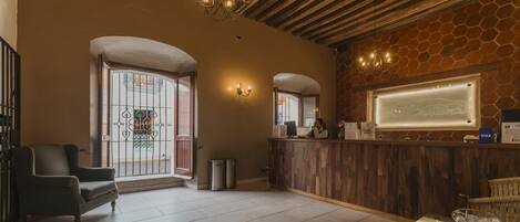 A reception area with a wooden reception desk, a chair, a glass door with a metal gate, and a chandelier.