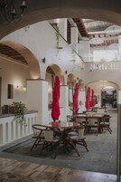 An indoor dining area with tables and chairs, red umbrellas, and a staircase leading to an upper level.