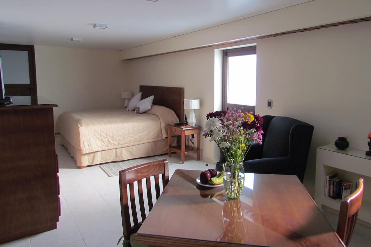 Quarto de hotel com cama, escrivaninha, cadeira, mesa com um vaso de flores e janela.