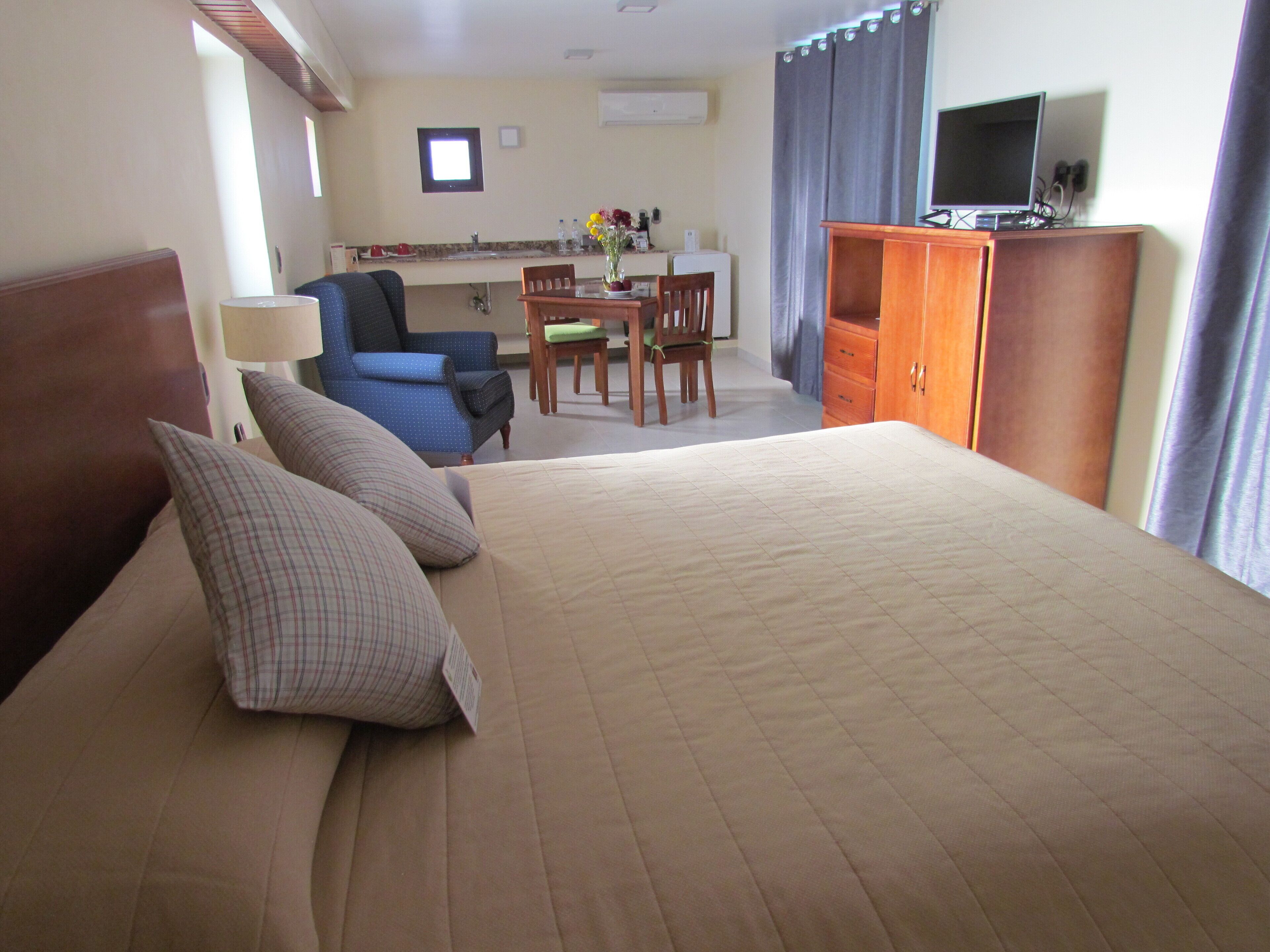 Quarto de hotel com uma cama grande, uma mesa com cadeira, televisão e guarda-roupa.