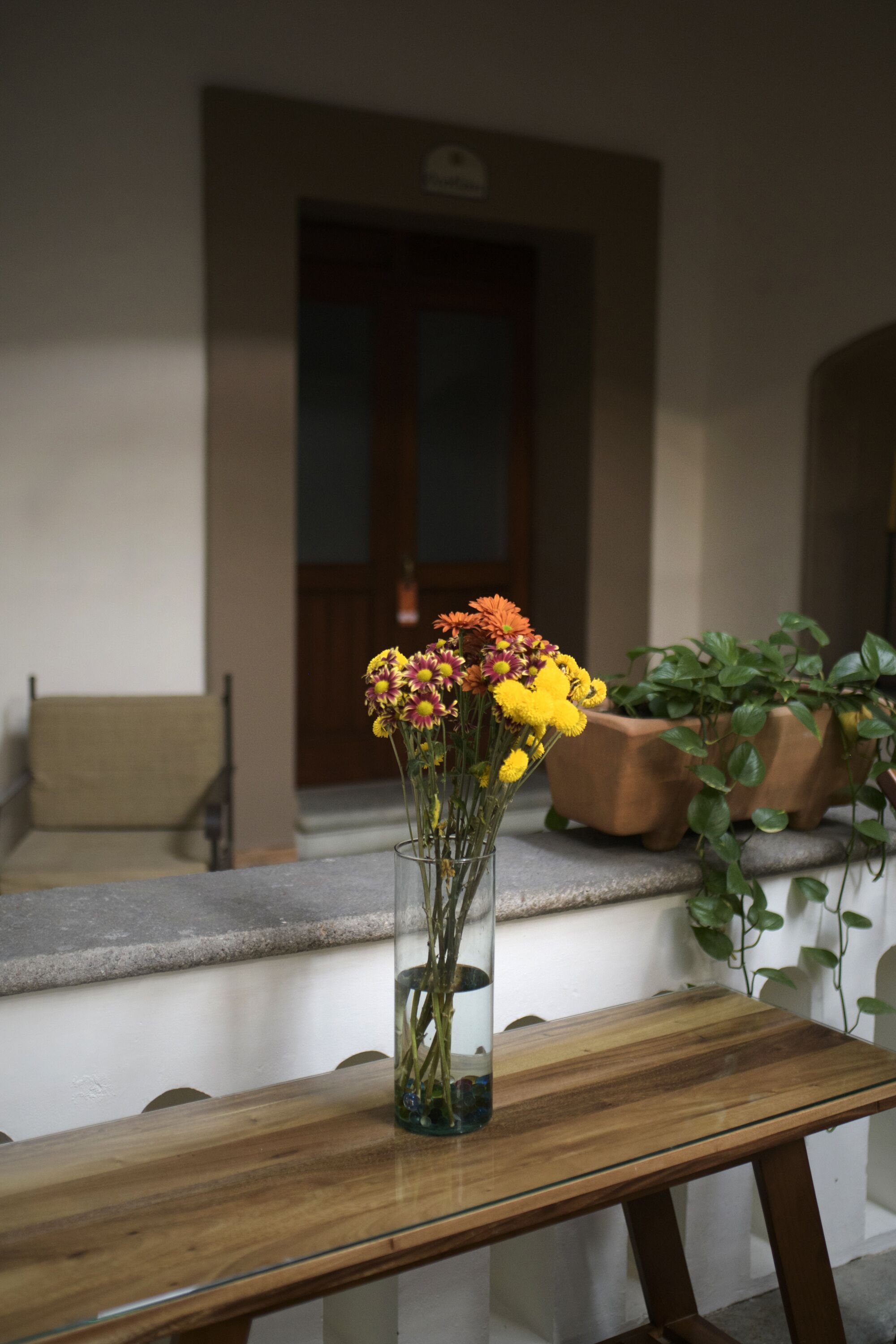 A wooden bench with a glass vase containing yellow flowers.