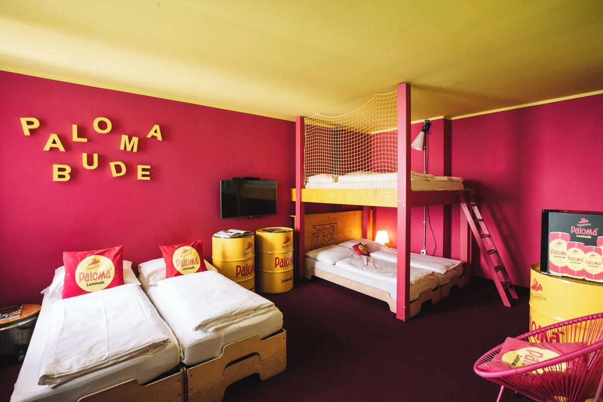 A room with bunk beds, a ladder, a TV, and a Paloma Bude branded pillow.