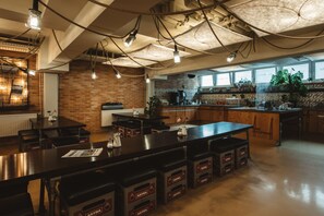 A modern kitchen with a brick wall, wooden cabinets, and a large island with stools. - Superbude St. Georg (Hamburg)