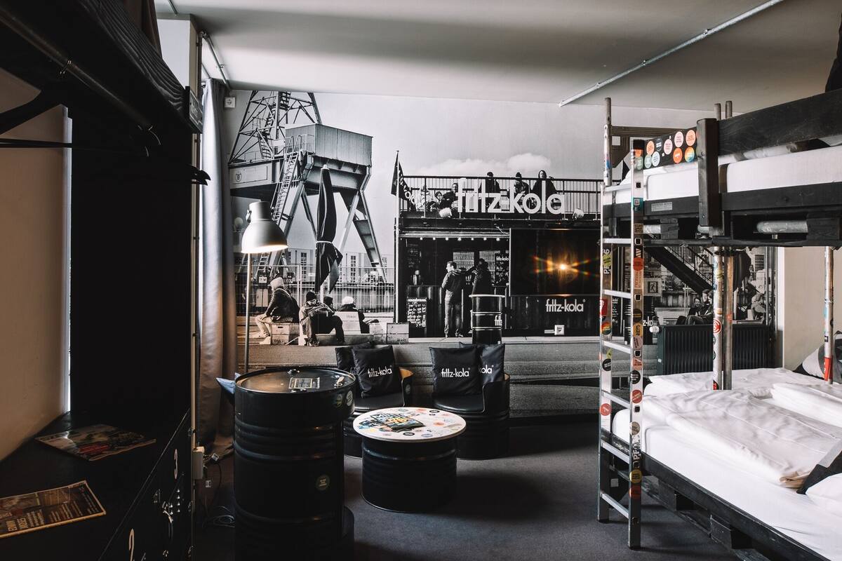 A compact, industrial-style room with bunk beds, a small seating area, and a large mural of a bridge.