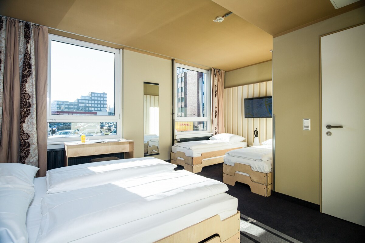 A hotel room with two beds, a desk, a television, and a window with a city view.