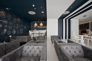 A modern lounge area with grey upholstered sofas, a bar with bottles, and a staircase leading to another level. - Maçarico Beach Hotel (Mira)