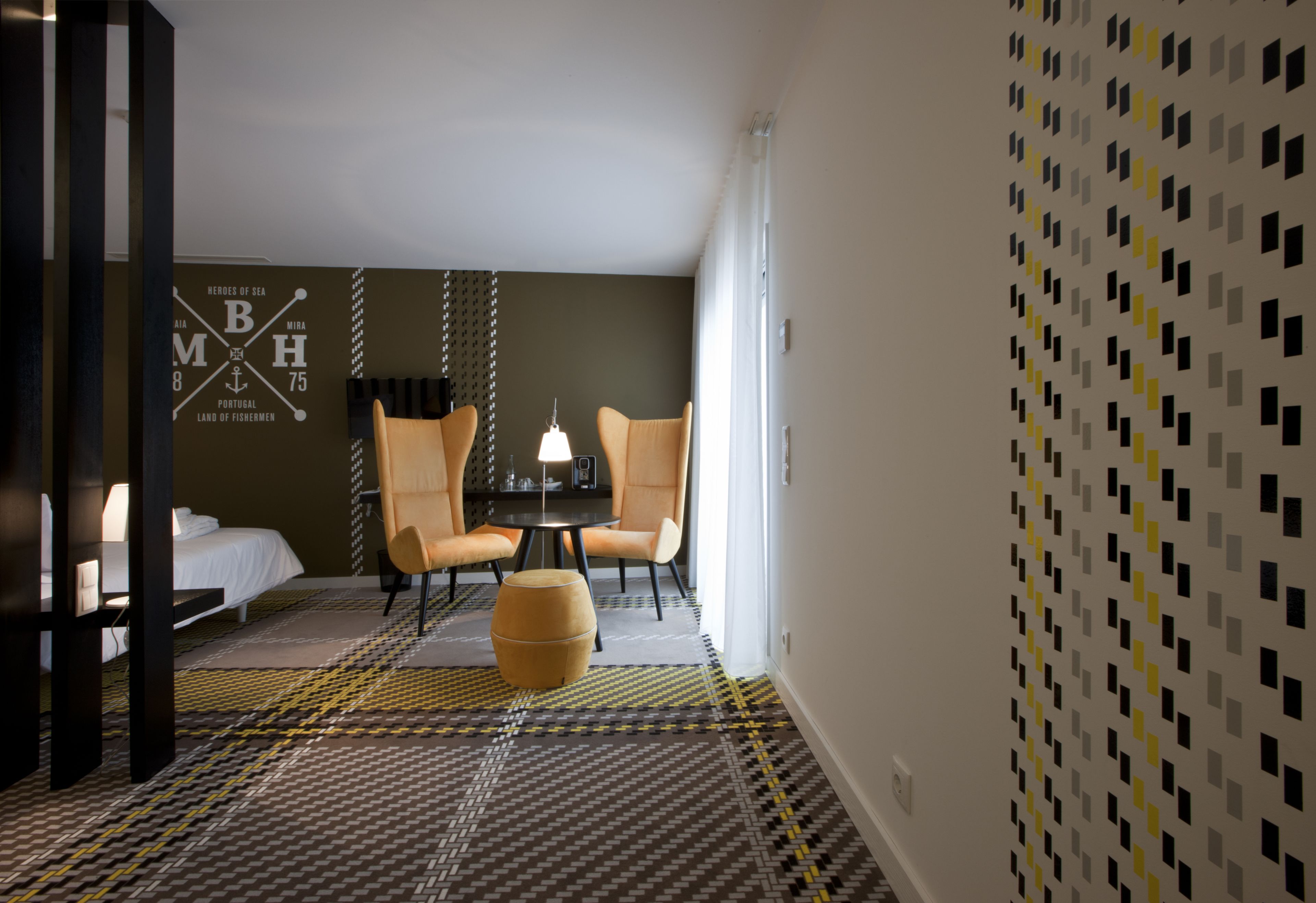 A hotel room with a bed, two chairs, a small table, and a patterned rug.