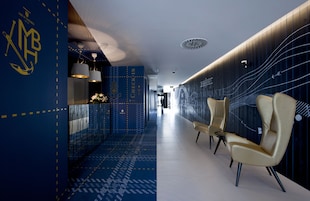 A modern hotel corridor with a check-in desk, seating area, and decorative wall patterns.