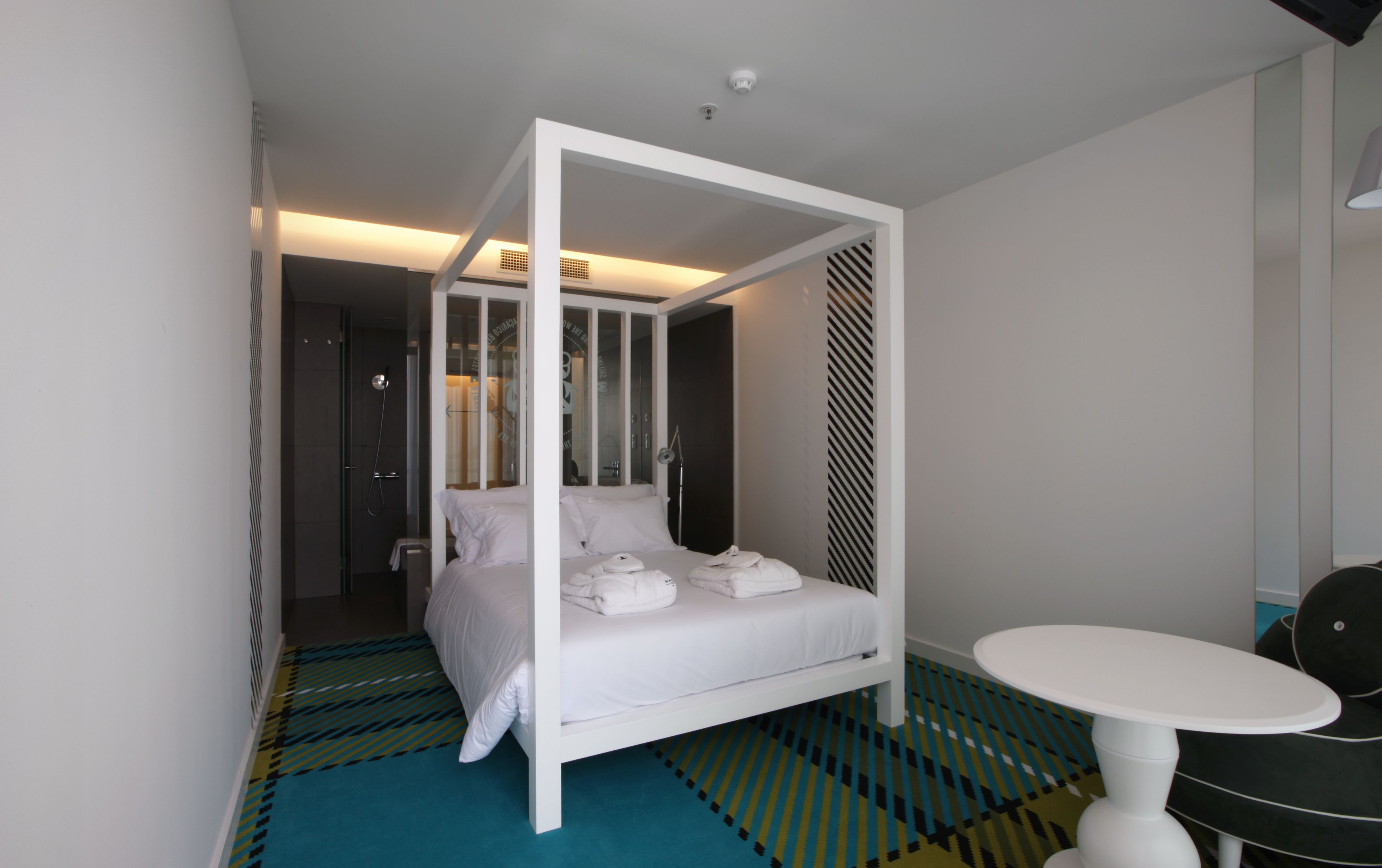 Quarto de hotel moderno com cama de dossel, uma pequena mesa redonda e um tapete estampado.