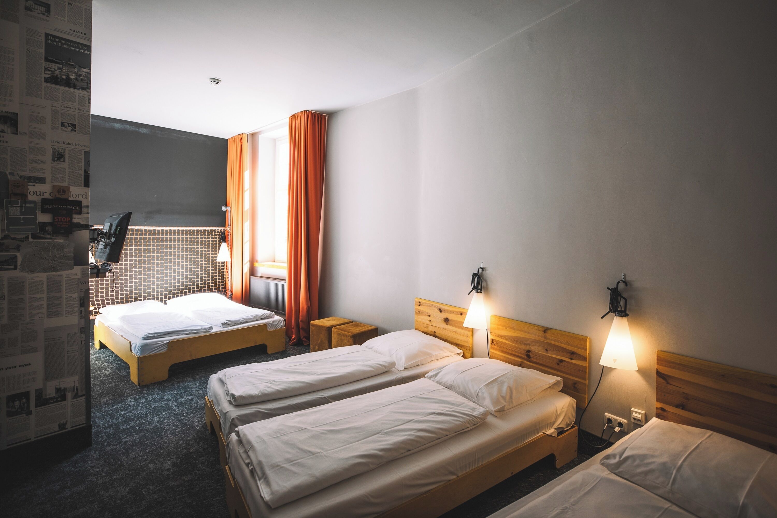 A hotel room with two single beds, a wooden headboard, a nightstand with a lamp, and a window with curtains.