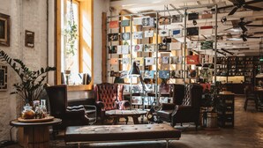 A cozy lounge area with leather furniture, a bookshelf filled with books and magazines, and a large window allowing natural light. - Superbude St. Pauli (Hamburg)