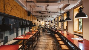 A restaurant with long wooden tables and booths, hanging pendant lights, and exposed ceiling beams. - Superbude St. Pauli (Hamburg)