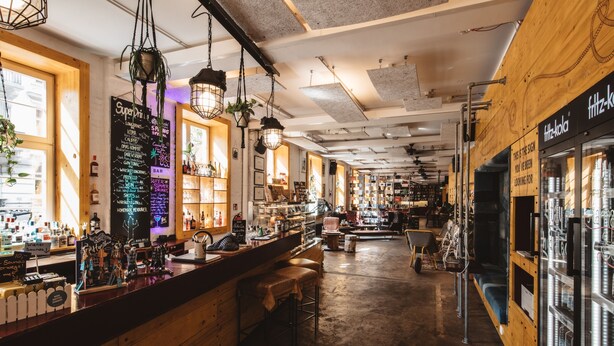 A bar with wooden walls, hanging lights, and a variety of bottles and glasses on shelves. - Superbude St. Pauli (Hamburg)
