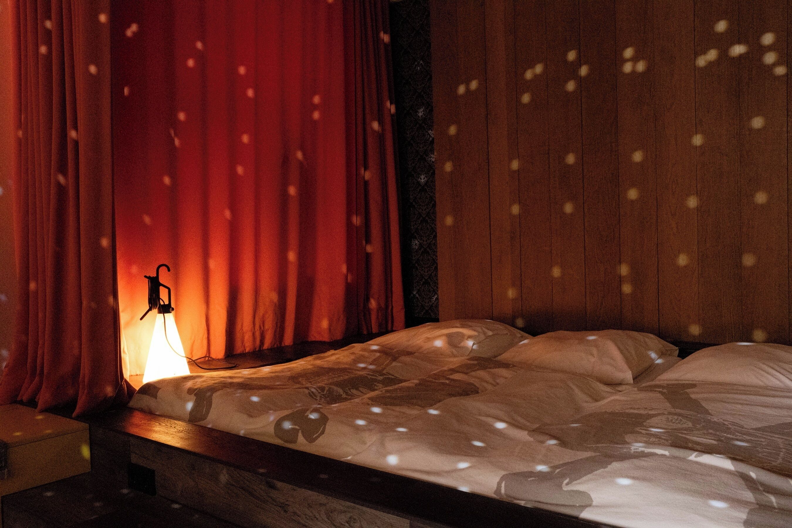 Un lit avec une couvre-lit à motifs, une table de chevet et une lampe fixée au mur.