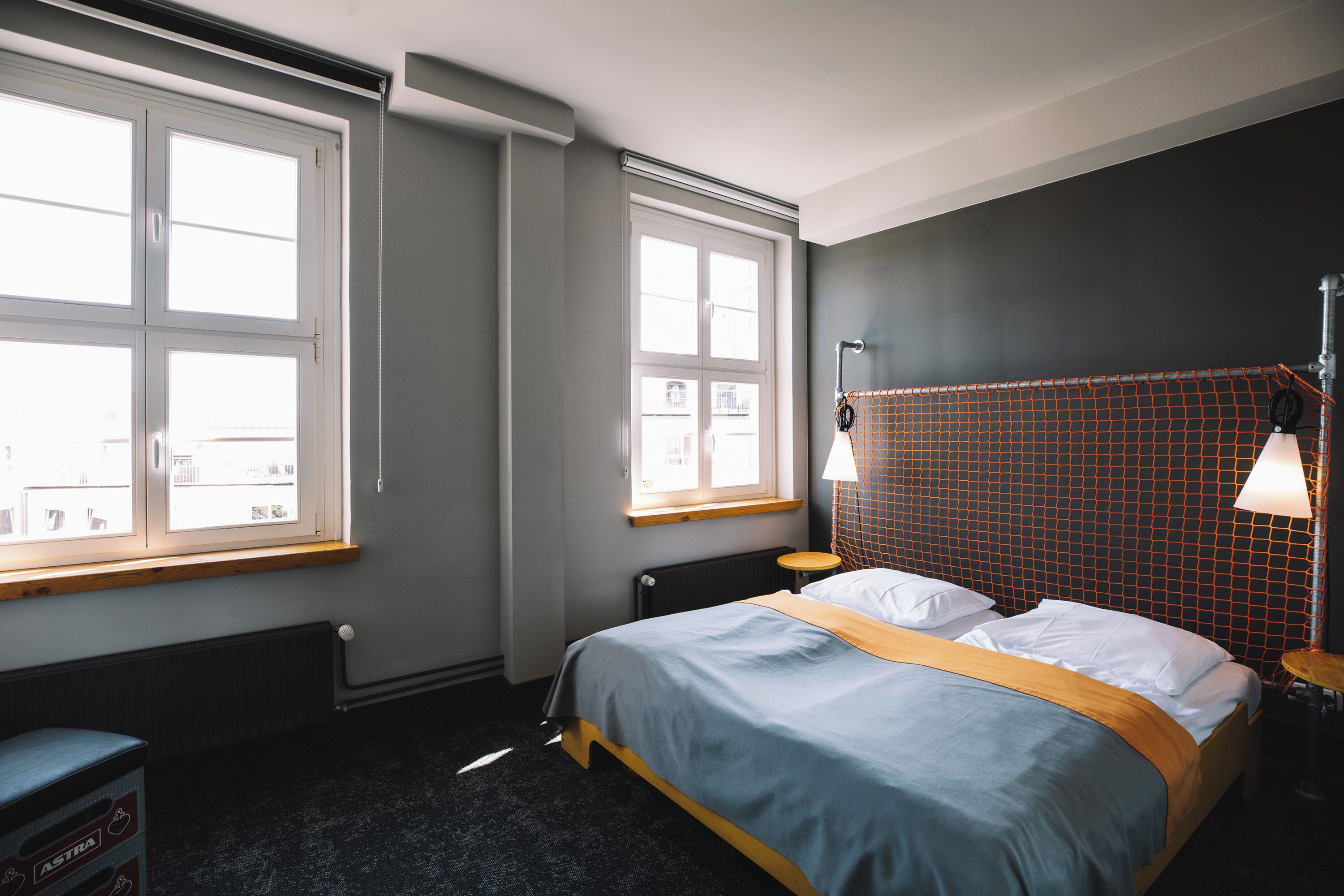 Ein Schlafzimmer mit einem Bett, zwei Fenstern, einem Heizkörper und einer Lampe.