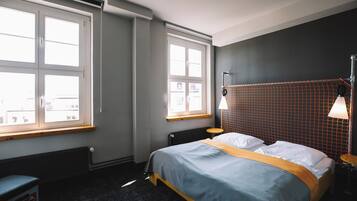 Ein Schlafzimmer mit einem Bett, zwei Fenstern, einem Heizkörper und einer Lampe.
