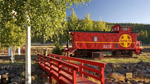 A red Santa Fe train caboose with the number 336, AT&SF 999336, and CE-2 on a track with a red bridge over rocks. - Canyon Motel and RV Park (Williams)