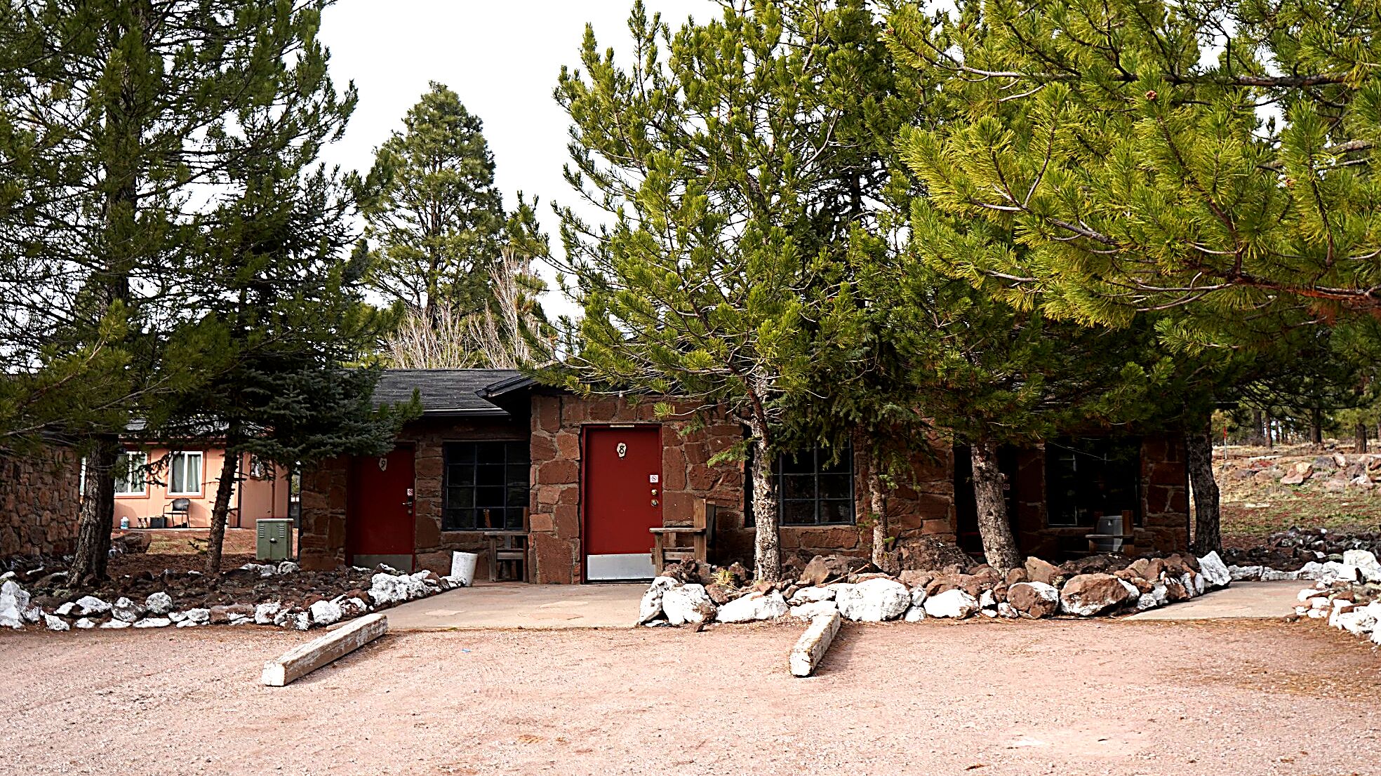 A rustic cabin with a stone exterior, a red door, and a gravel driveway.