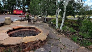A stone fire pit with outdoor seating, surrounded by birch trees and a stone pathway. - Canyon Motel and RV Park (Williams)