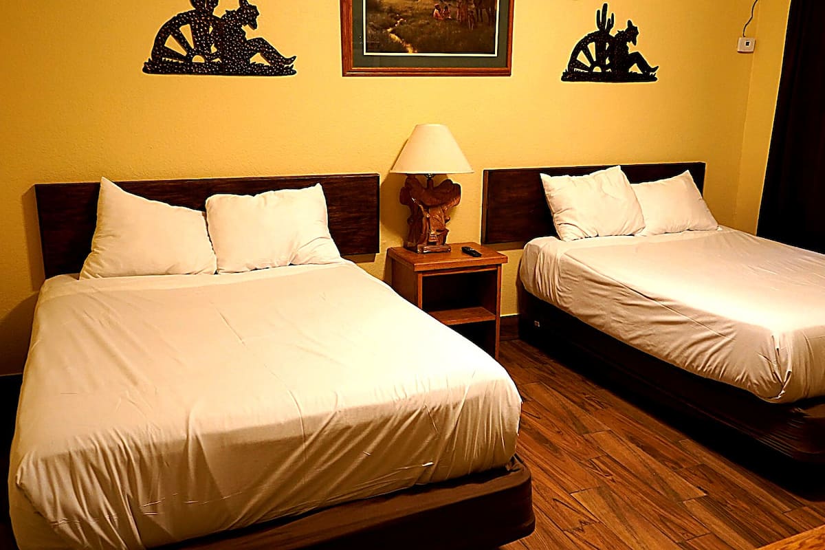 Ein Hotelzimmer mit zwei Betten, einem Nachttisch mit Lampe und Kunstwerken an den Wänden.