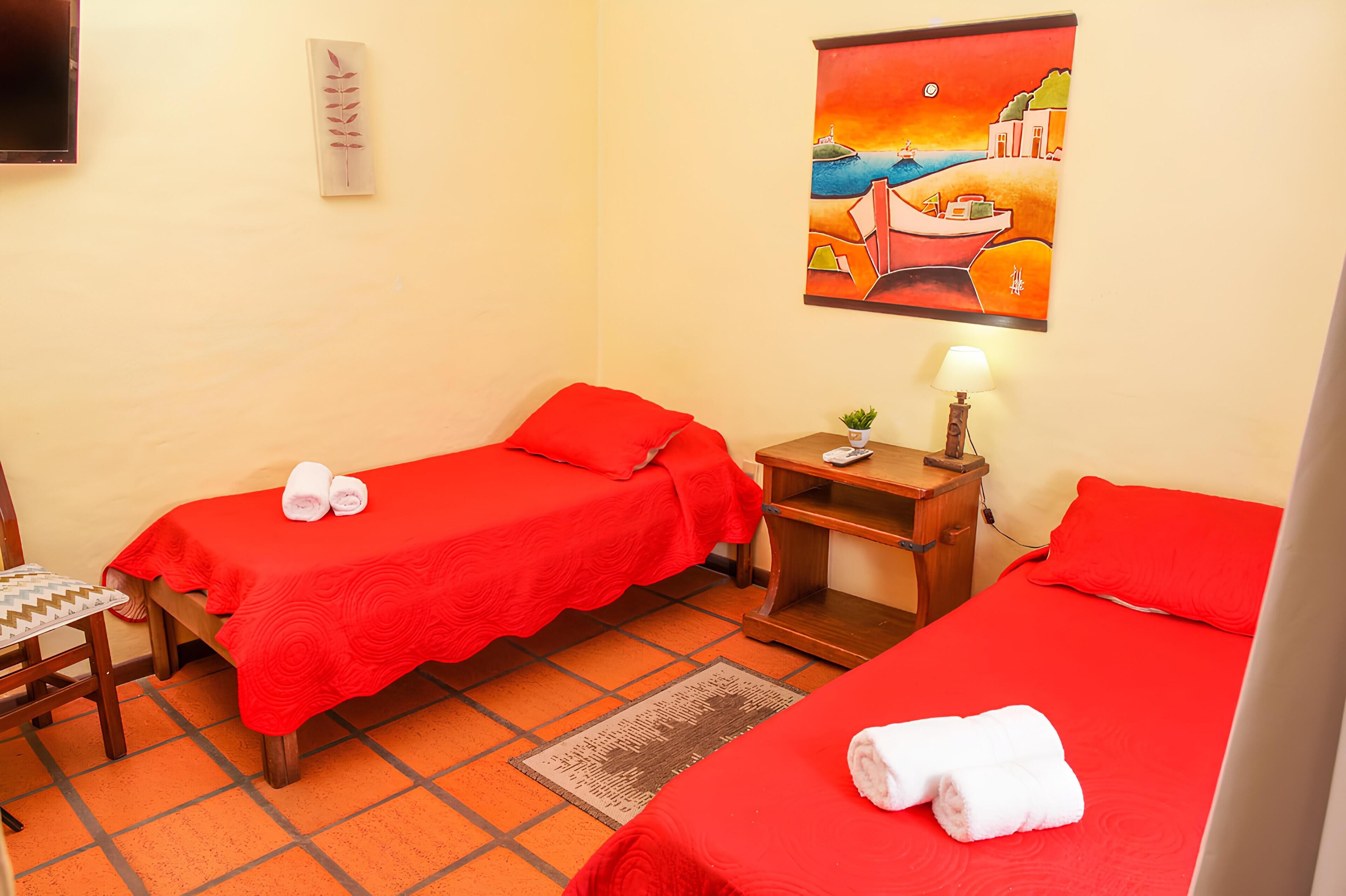 Una habitación de hotel con dos camas individuales, un escritorio pequeño con una lámpara, una silla y un cuadro en la pared.