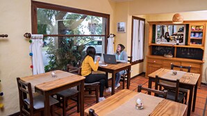 Un café acogedor con mesas y sillas de madera, un ventanal con cortinas y un menú en la pizarra.